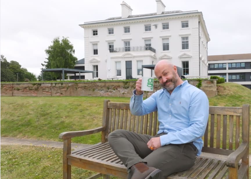 Simon Girling on a bench outside the Girling Jones office, raising a GJ mug